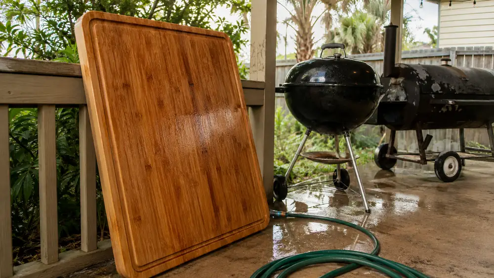 A large bamboo carving board leaning against a porch rail, dripping wet after being hosed down outdoors