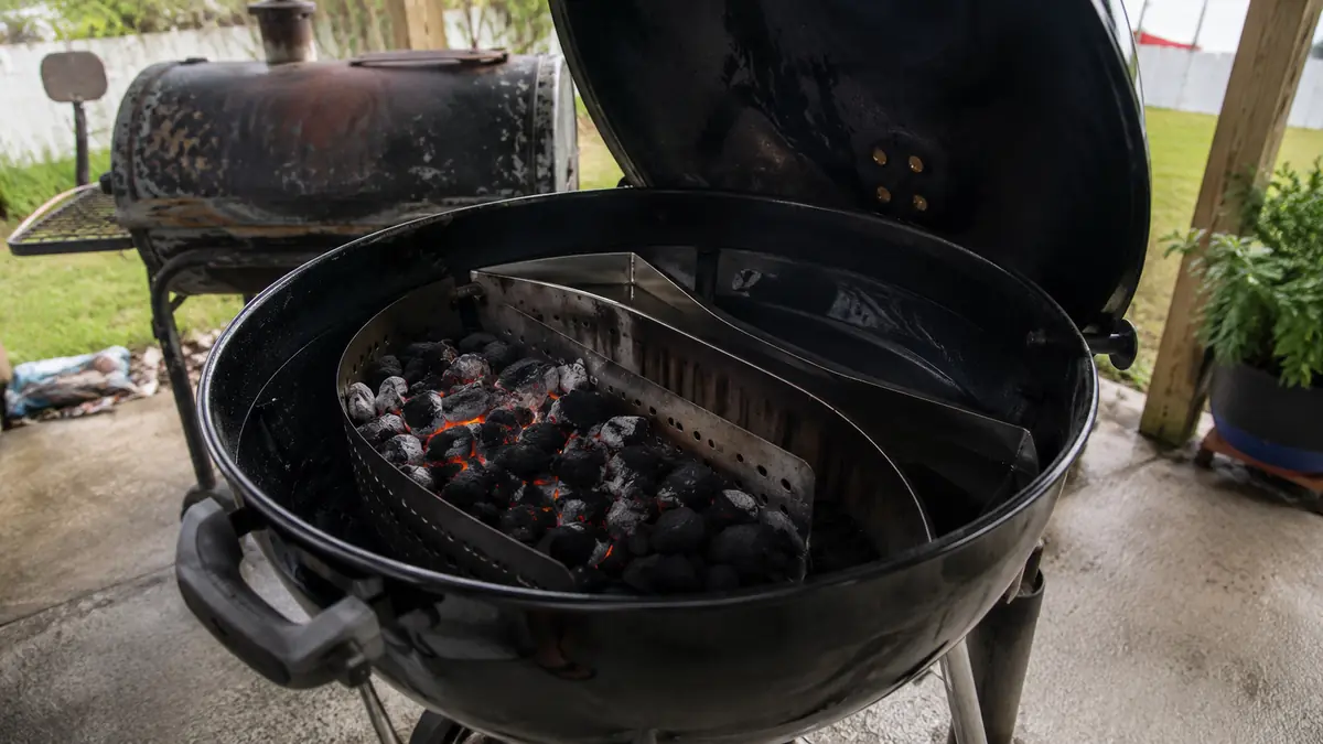 A stainless charcoal basket insert loaded and glowing inside an open 22-inch kettle grill on a patio
