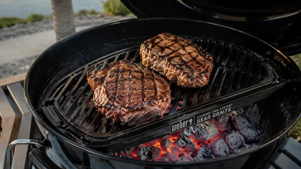 Close-up of ribeyes with deep dark crosshatch sear marks resting on a black porcelain-enameled cast iron sear grate